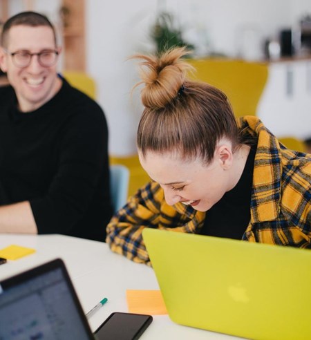 People laughing working on laptop in office